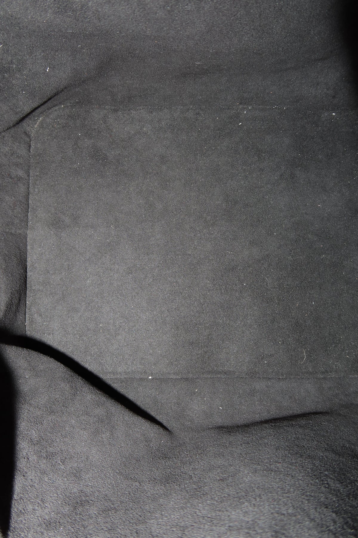 Close-up of a dark gray suede or microfiber fabric surface with a stitched rectangular pocket and a dark seam running diagonally.
