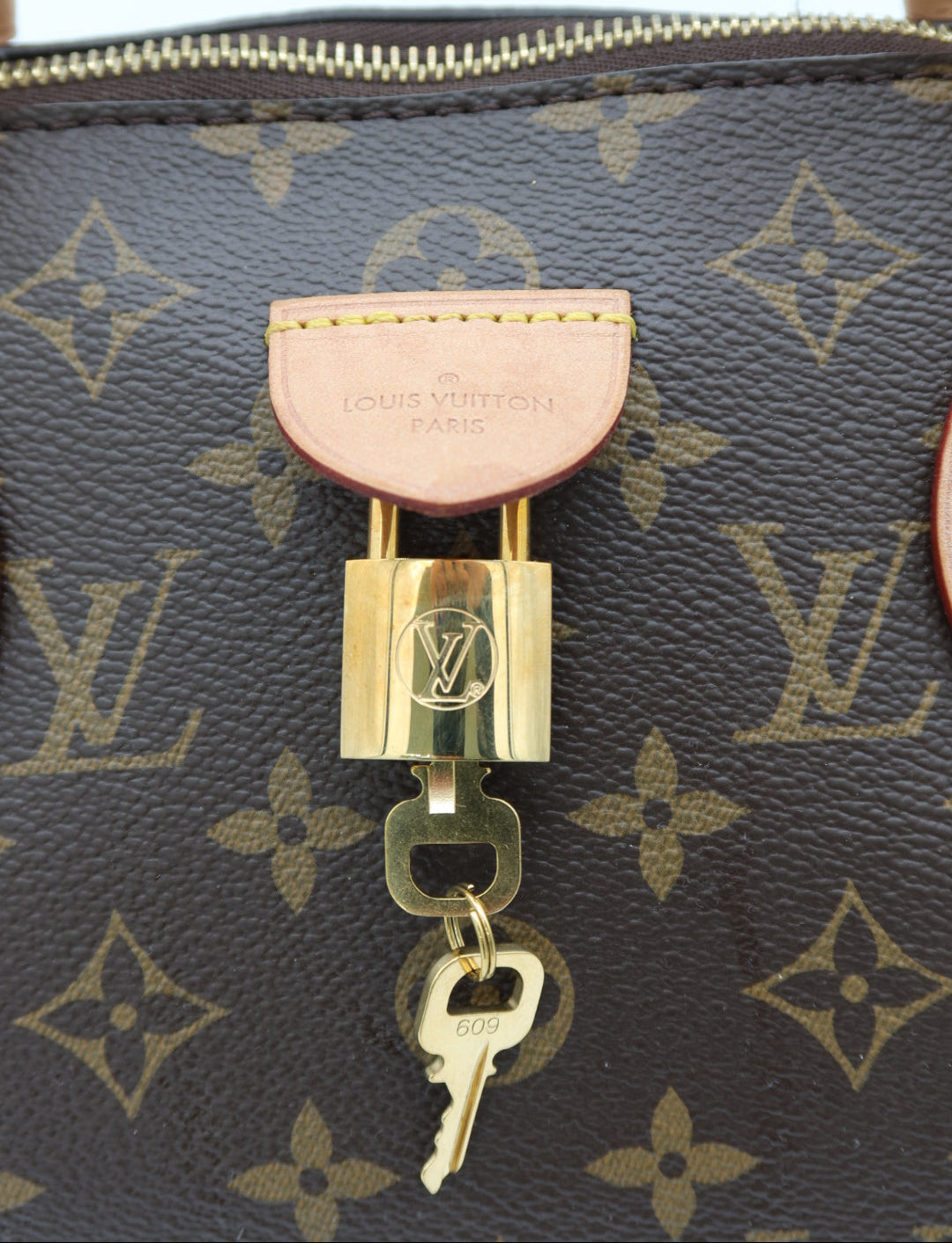 Close-up of a Louis Vuitton monogram bag with a gold padlock and key closure, featuring the brand's signature brown canvas and tan leather details.