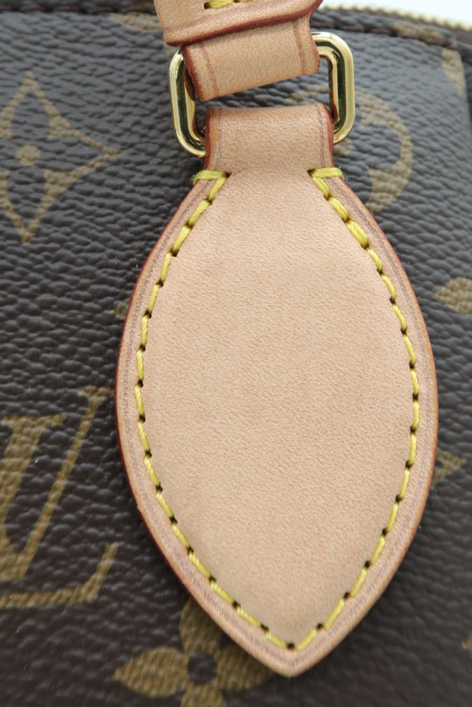 Close-up of a Louis Vuitton monogram handbag showing the signature brown coated canvas with gold-tone LV monogram pattern, a beige leather strap, and a matching beige leather teardrop-shaped tag with yellow contrast stitching.