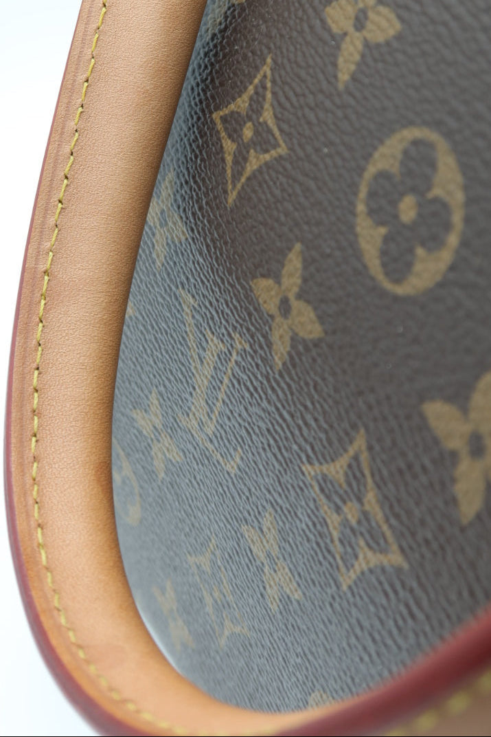Close-up of a Louis Vuitton handbag corner showing the brown monogram canvas and tan leather trim against a white background.