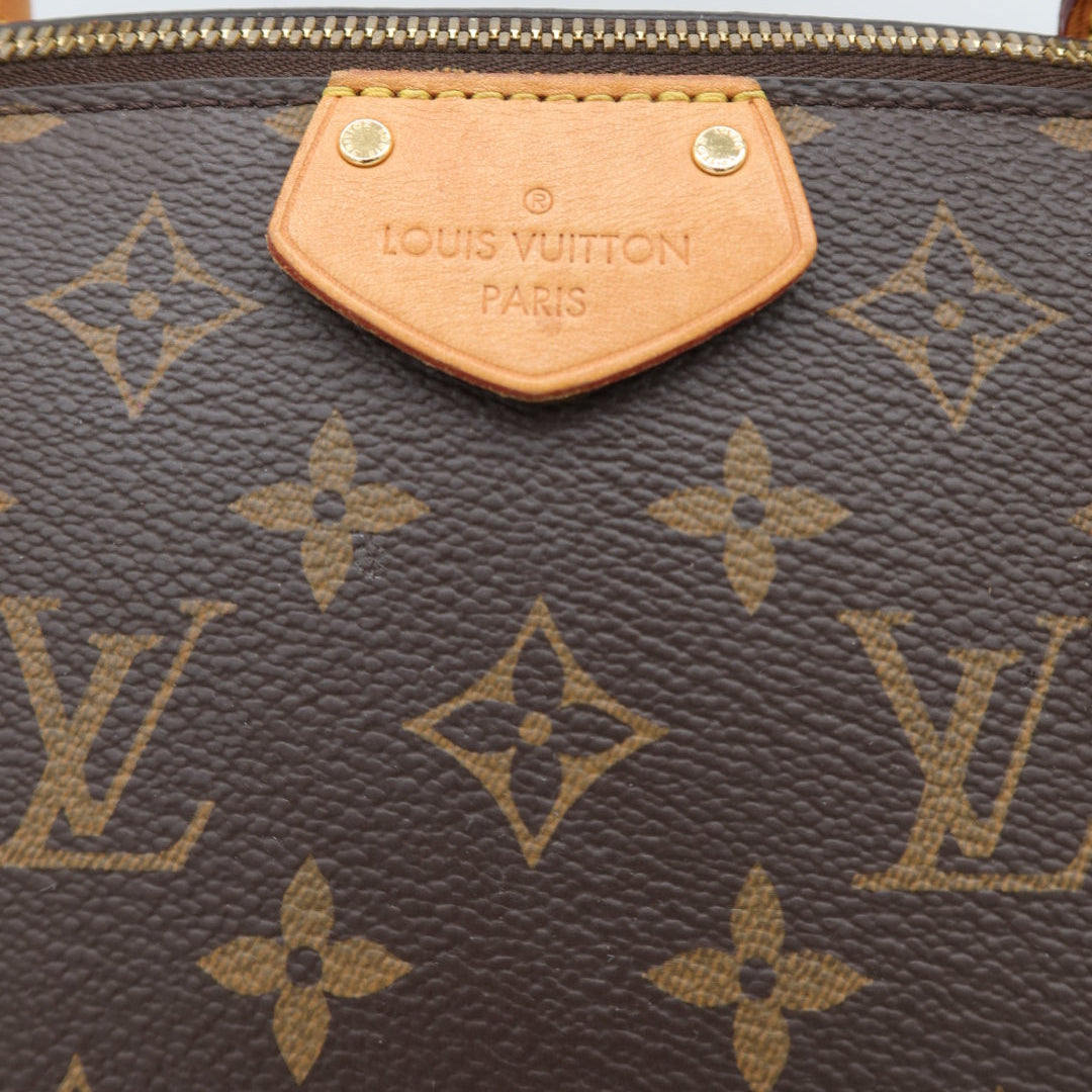 Close-up of a Louis Vuitton monogram canvas bag with a tan leather logo tab and gold-tone hardware on a white background.