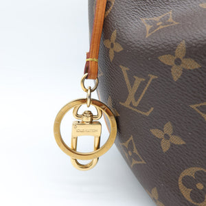 Close-up of a Louis Vuitton monogram bag in dark brown coated canvas with gold-tone hardware and a small hanging keychain charm engraved with the Louis Vuitton name.