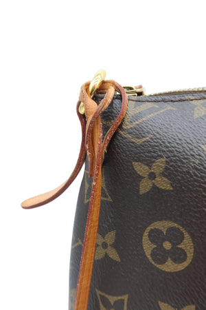 Close-up of a Louis Vuitton monogram canvas bag with a brown leather zipper pull and gold-tone hardware against a light blue background.