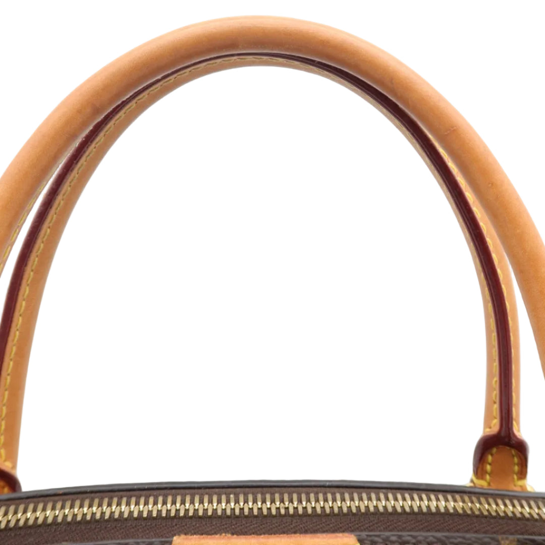 Close-up of a handbag handle in tan leather against a white background, with part of the dark monogram canvas body and gold zipper visible at the bottom.