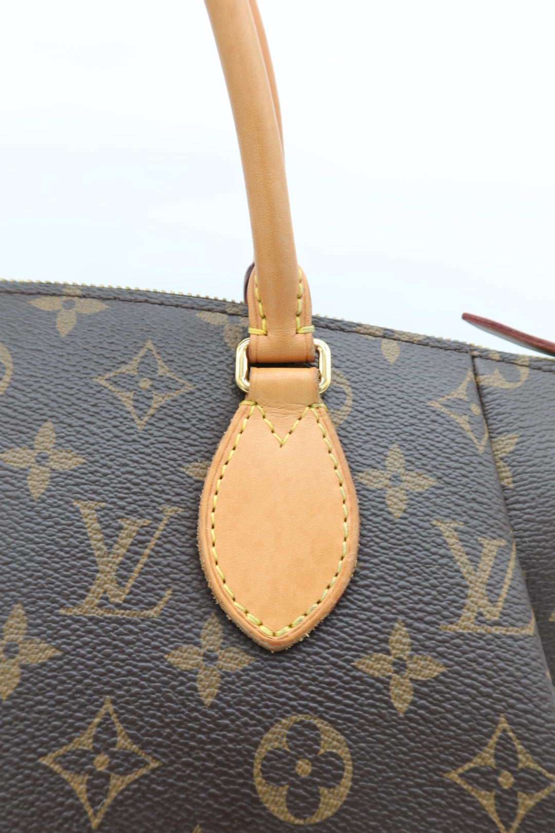Close-up of a Louis Vuitton monogram handbag showing the dark brown coated canvas with tan monogram print, a tan leather handle attachment, and gold-tone hardware.