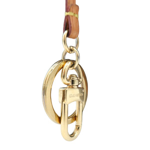 Close-up of a Louis Vuitton monogram bag in dark brown coated canvas with gold-tone hardware, featuring a gold-tone oval ring clasp and a tan leather strap on a white background.