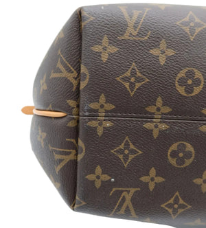 Close-up of a Louis Vuitton monogram canvas bag corner showing the classic brown and tan LV pattern with a small tan leather pull tab on a white background.