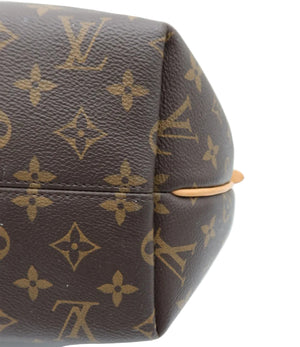 Close-up of a Louis Vuitton monogram canvas bag corner showing the brown coated canvas with tan monogram motifs and a light tan leather edge.