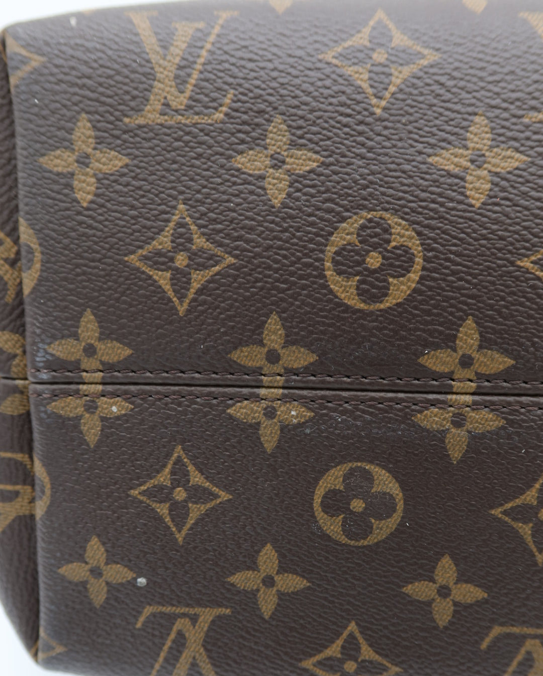 Close-up of a brown monogram canvas bag with tan Louis Vuitton-style LV and floral motifs, showing part of the body and a horizontal seam.