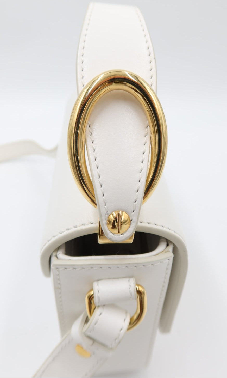 Close-up of a white leather handbag featuring a prominent gold-tone O-ring clasp and matching gold hardware on a clean white background.