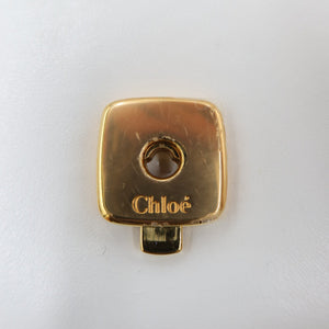 A gold-tone metal hardware piece with the brand name 'Chloé' engraved on it, set against a plain white background.
