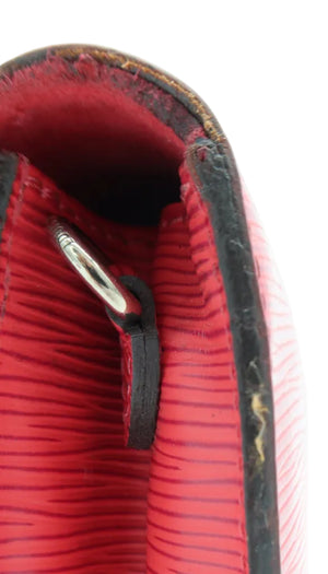 Close-up detail of a red textured leather clutch or wallet showing the interior lining, black edge trim, and a silver metal snap closure on a white background.