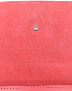 A close-up of a coral pink suede wallet or clutch showing the interior lining and a small silver metal snap button closure.