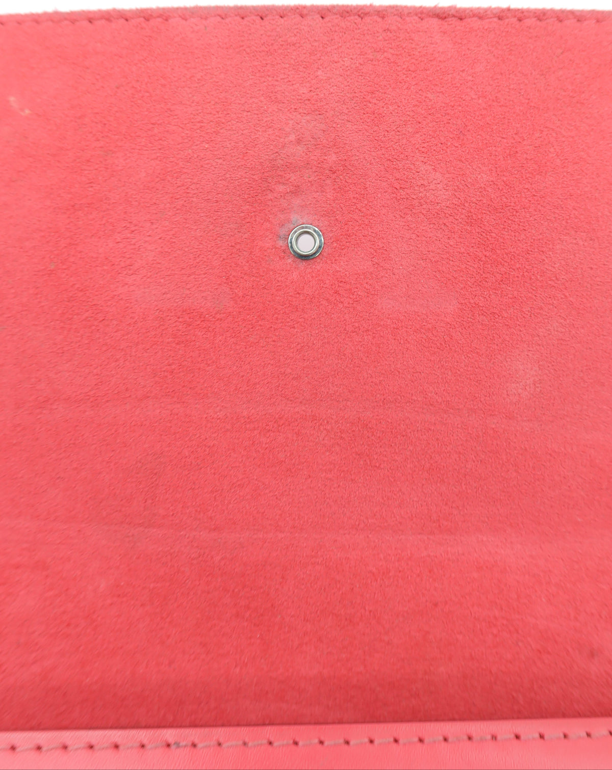 A close-up of a coral pink suede wallet or clutch showing the interior lining and a small silver metal snap button closure.