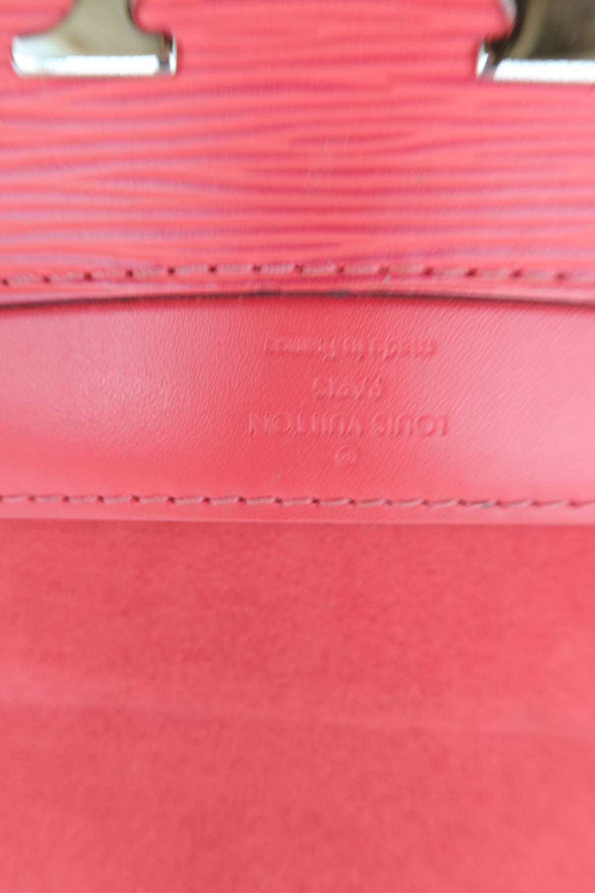 Close-up detail of a pink Louis Vuitton handbag showing the textured Epi leather strap, fine stitching, and embossed brand lettering on the leather tab.