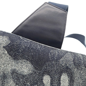 Close-up of a shoulder bag showing a dark navy blue leather strap attached to a gray and black speckled canvas body, set against a plain white background.