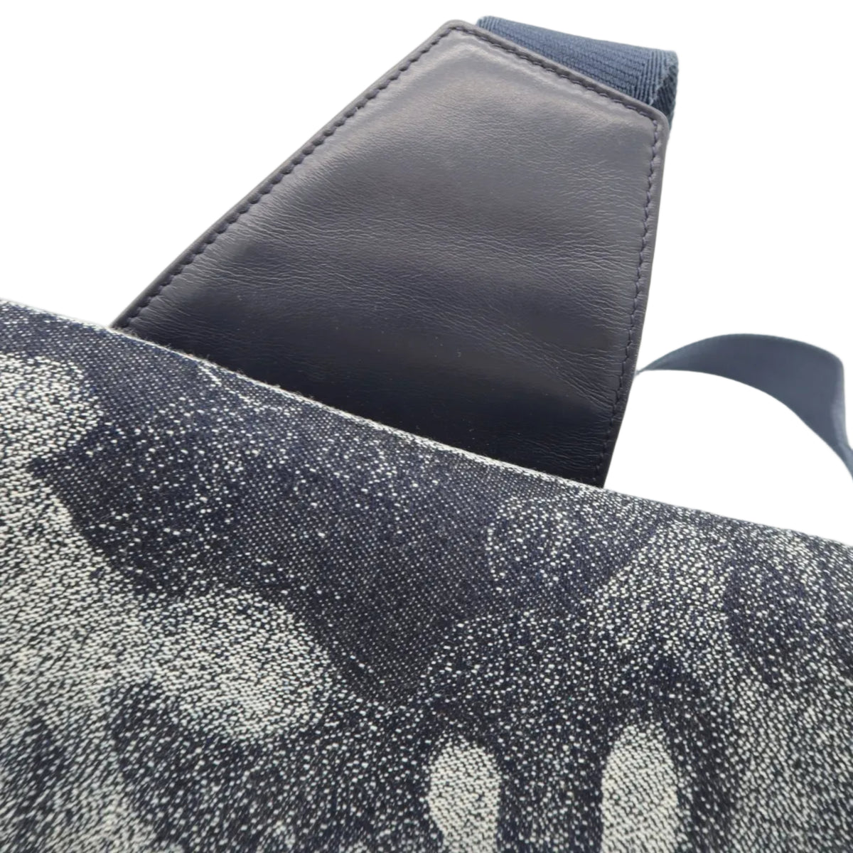Close-up of a shoulder bag showing a dark navy blue leather strap attached to a gray and black speckled canvas body, set against a plain white background.