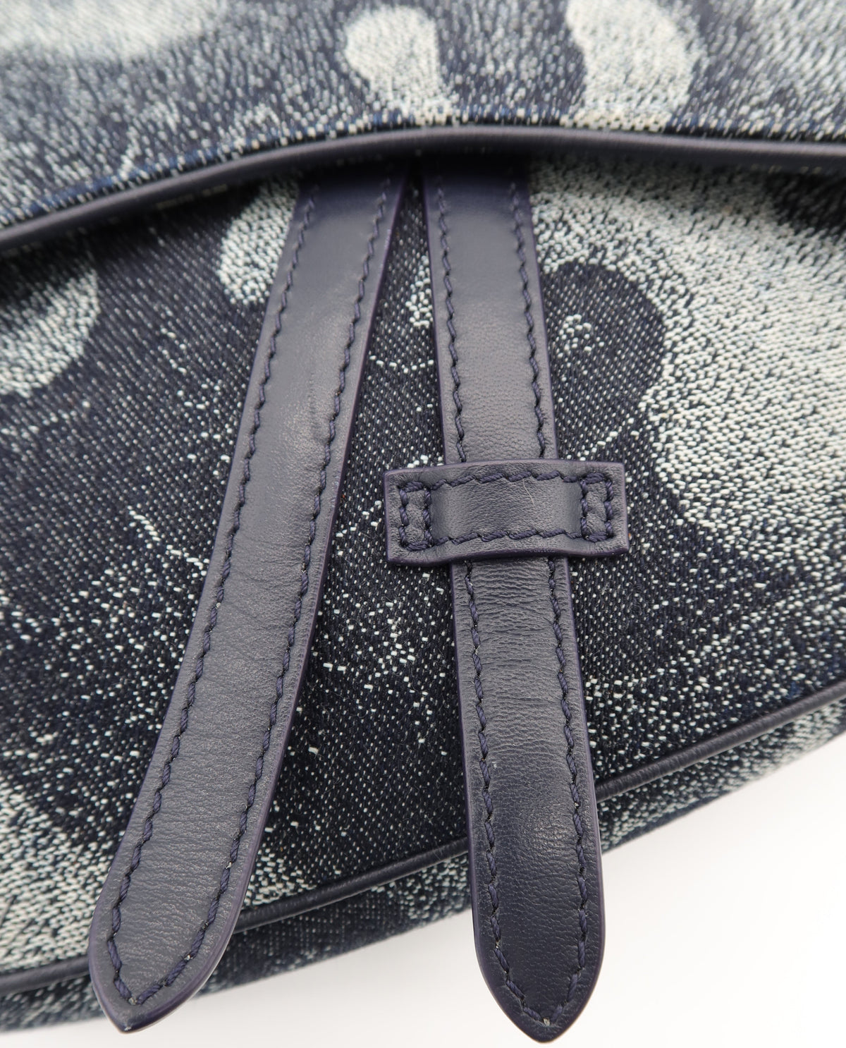 Close-up of a textured canvas bag with a dark navy blue leather strap and trim, featuring a gray and white abstract pattern.