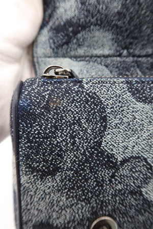 Close-up of a textured denim bag with a dark blue and gray abstract pattern, featuring silver-tone metal hardware.