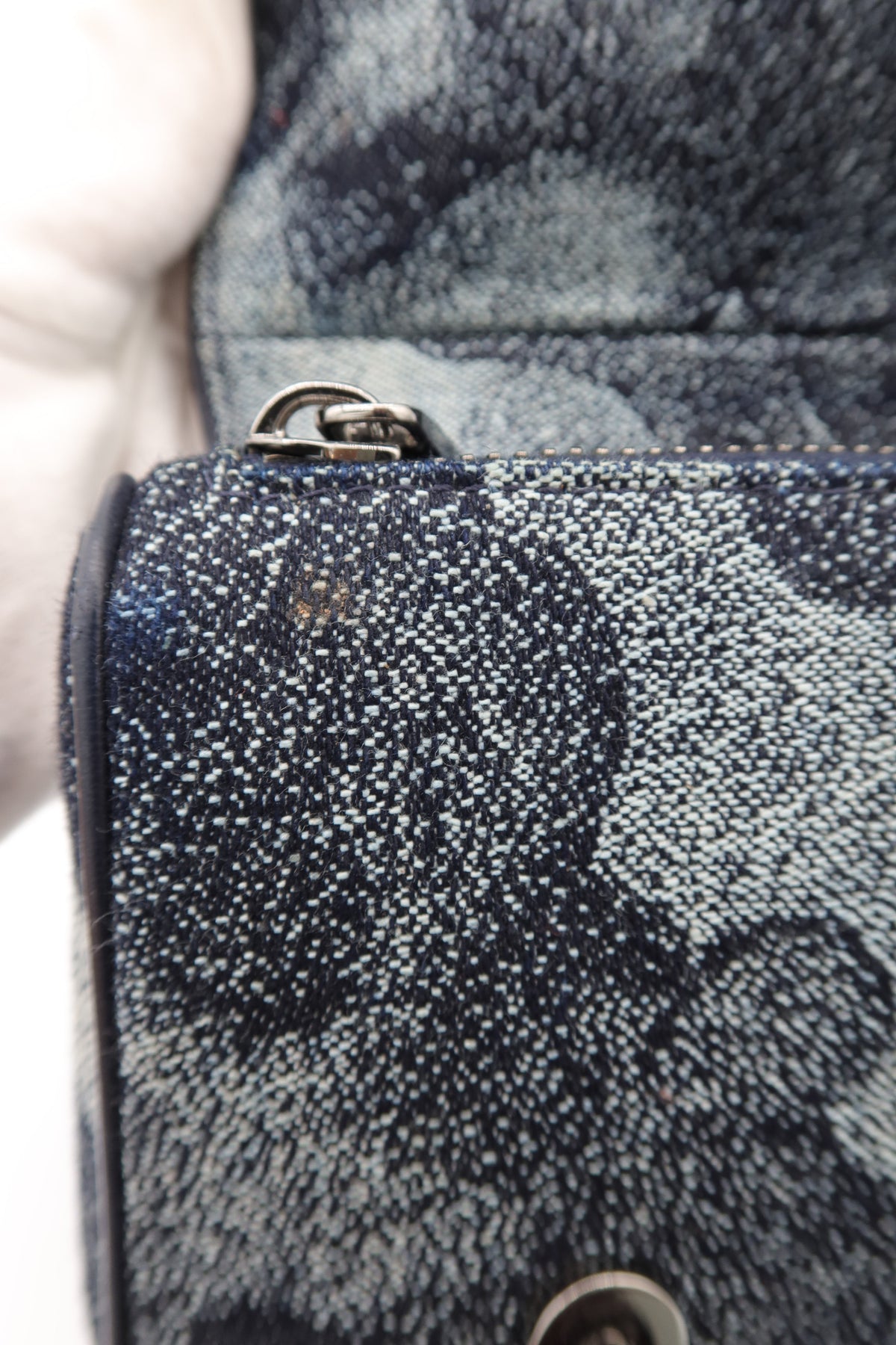 Close-up of a textured denim bag with a dark blue and gray abstract pattern, featuring silver-tone metal hardware.
