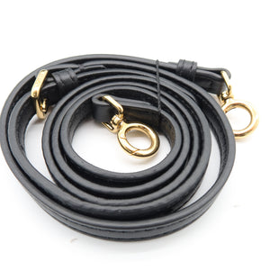 A black leather shoulder strap coiled on a white background, featuring gold-tone metal hardware including rings and clips.