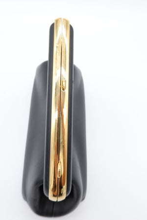 A close-up of a black leather clutch bag with a prominent, polished gold-tone metal accent running horizontally across the center.
