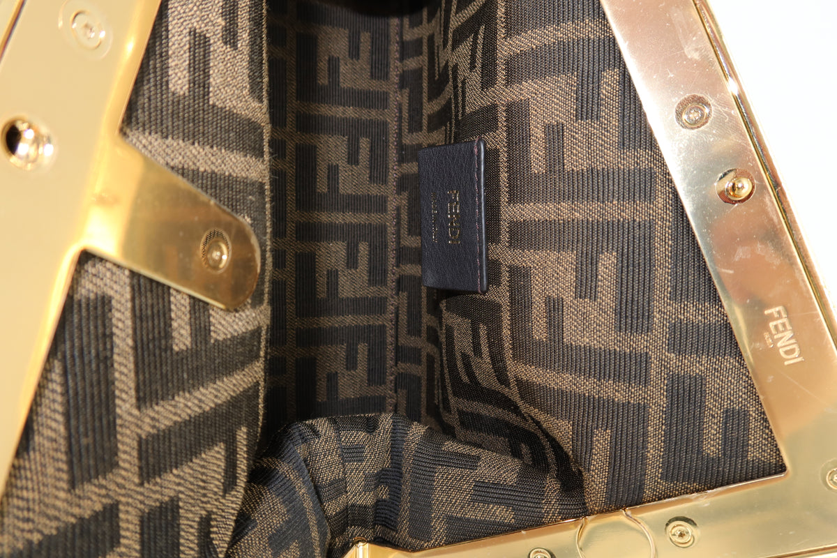 Close-up of the interior of a Fendi handbag, showing the signature brown and beige FF monogram canvas lining and polished gold-tone hardware with a small Fendi brand tag.