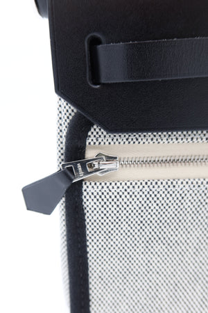 Close-up of a textured black and white patterned bag with a black leather strap and a silver zipper pull.