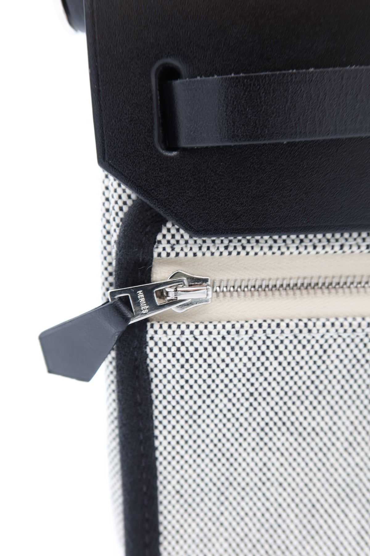 Close-up of a textured black and white patterned bag with a black leather strap and a silver zipper pull.
