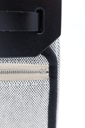 Close-up detail of a black leather strap attached to a black-and-white patterned fabric pouch with a silver zipper.