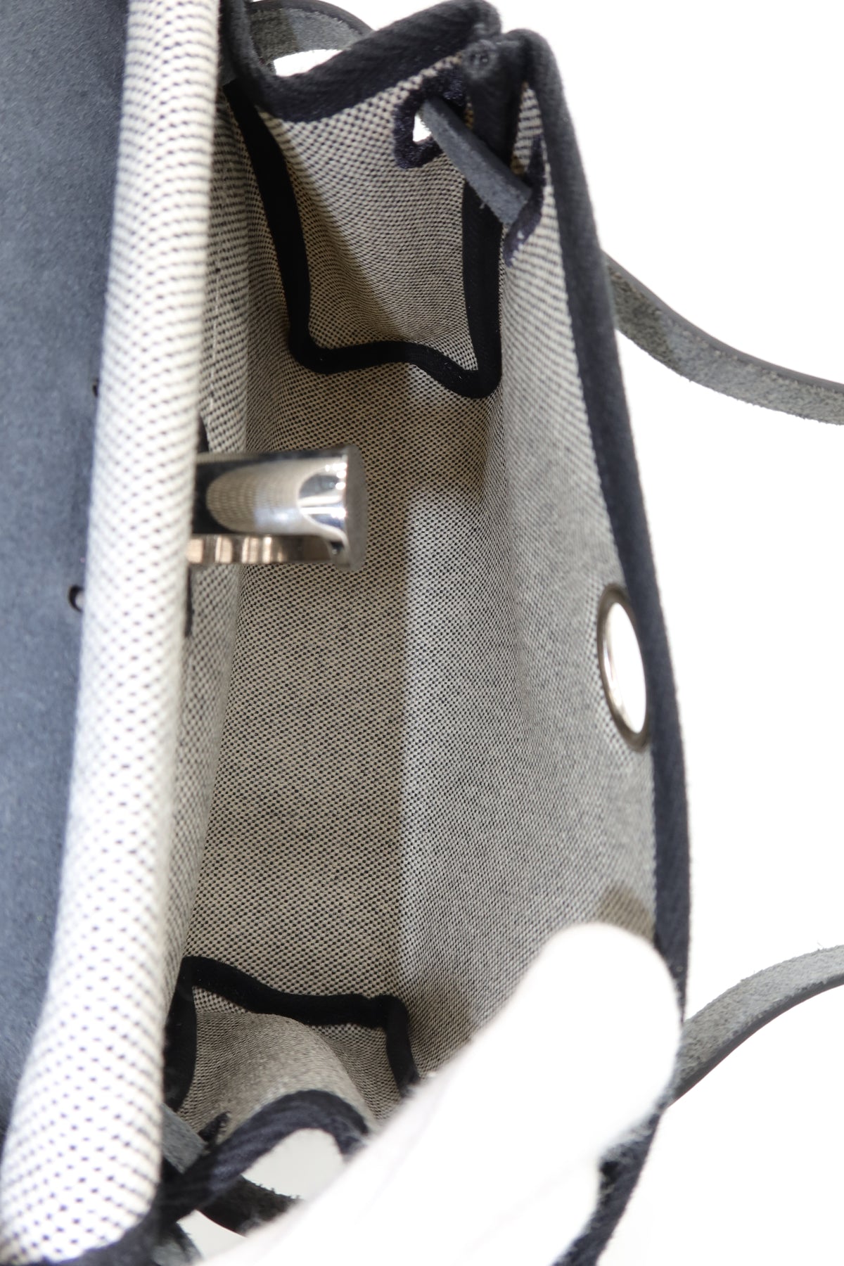 Close-up of the interior of a gray woven tote bag with black trim, metal grommets, and a white textured fabric panel.