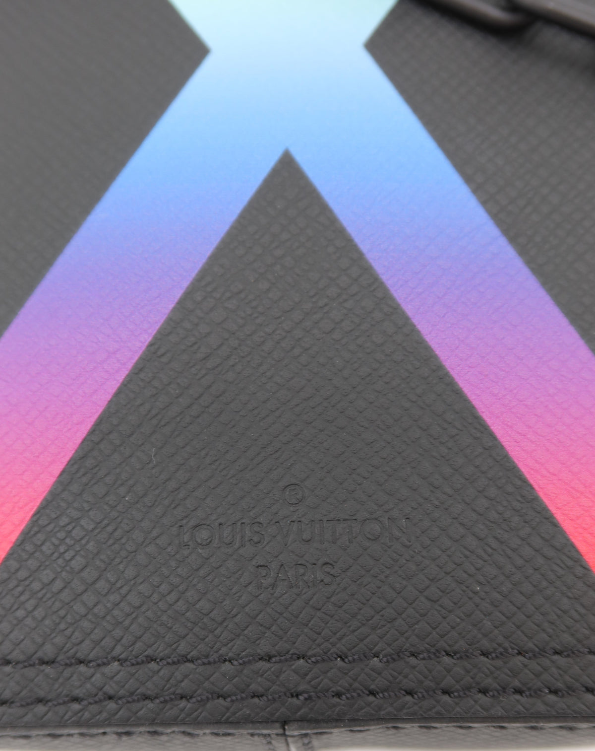 Close-up of a Louis Vuitton monogram bag in black textured leather with a vibrant blue, purple, and pink gradient X logo on a white background.