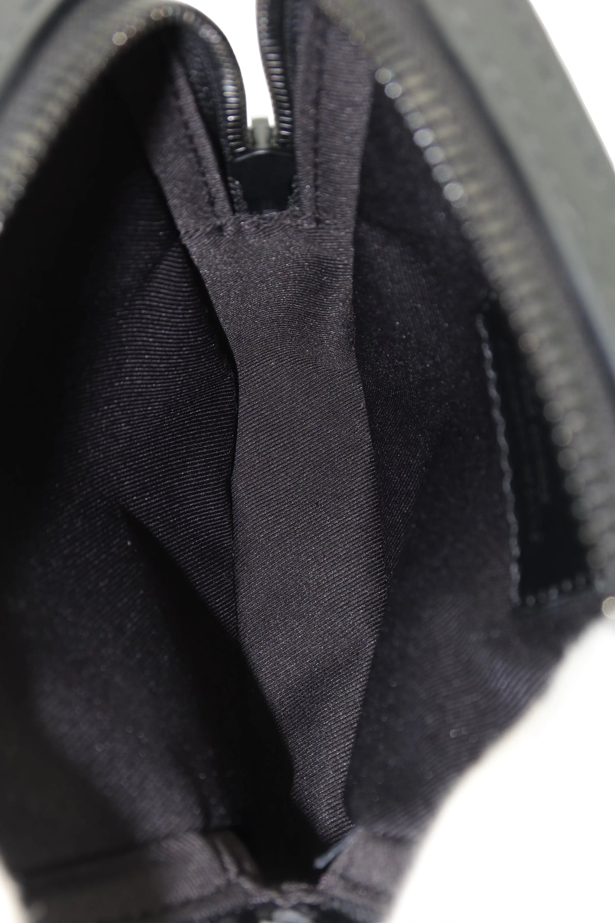 Close-up of the interior of a black zippered pouch or small bag, showing a dark fabric lining and zipper track against a white background.