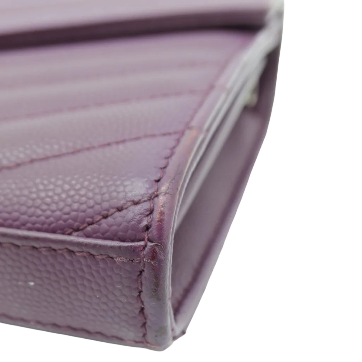 A close-up shot of a purple pebbled leather wallet corner, showing the texture and stitching against a white background.