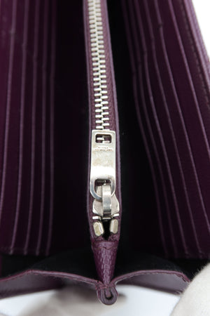 Close-up of a dark purple leather zippered wallet or clutch with a silver metal zipper pull and card slots inside.
