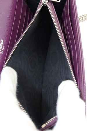 Close-up of a purple leather shoulder bag with silver zippers, showing the black patterned interior lining and a white-gloved hand holding it open.
