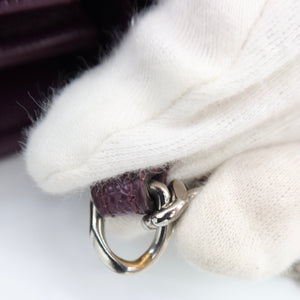 A close-up of a white knit glove holding a silver metal D-ring attachment next to a textured dark purple leather strap on a white background.