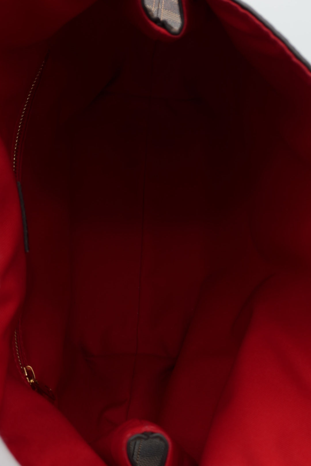 Close-up view of the interior lining of a red tote bag, showing the red fabric interior, a zipper track, and a small portion of the dark exterior fabric at the top and bottom edges.