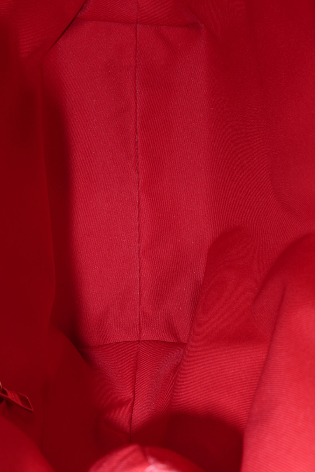 A close-up view of a bright red fabric surface with visible seams and folds, likely part of a garment or bag interior.