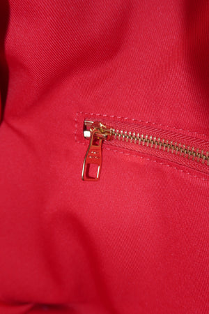 Close-up of a bright red fabric item featuring a gold-toned metal zipper with a pull tab.
