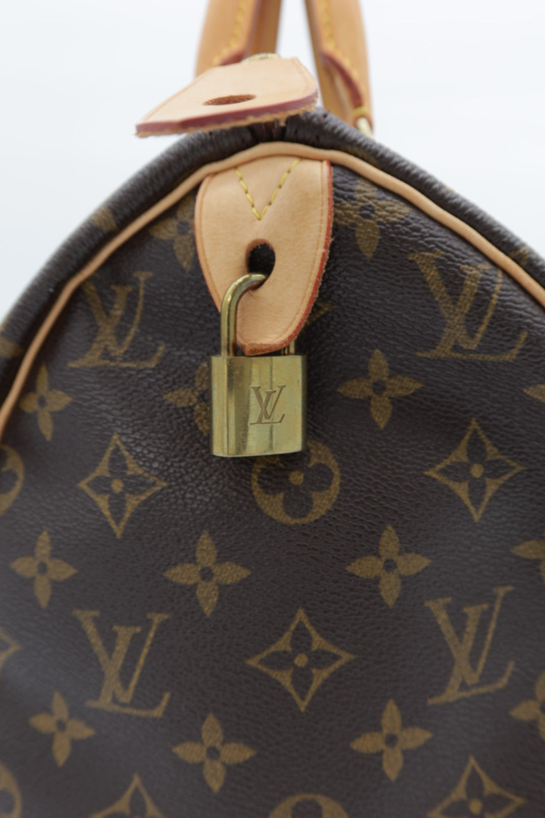 Close-up of a Louis Vuitton monogram bag in dark brown coated canvas with tan leather trim and a gold-toned padlock on a white background.
