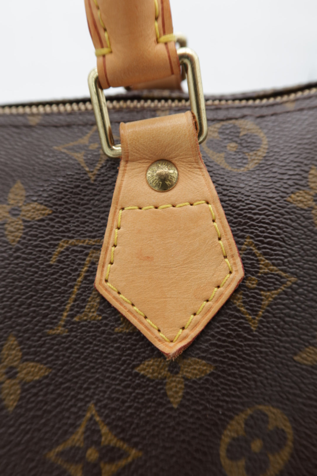 Close-up of a Louis Vuitton monogram handbag in dark brown coated canvas with tan leather trim and gold-tone hardware.