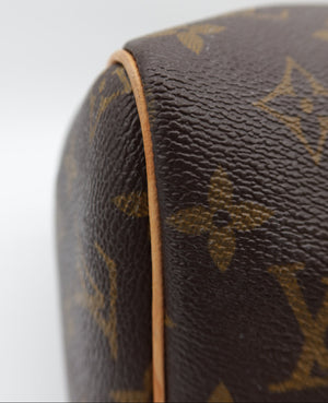 Close-up of a Louis Vuitton monogram coated canvas bag corner, showing the classic brown and tan LV pattern and a light tan leather edge against a white background.
