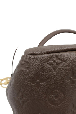 Close-up of a brown textured leather handbag with an embossed monogram pattern and a dark strap, photographed against a light gray background.