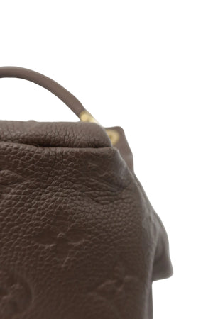 Close-up of a brown pebbled leather handbag corner with a small gold-tone hardware accent on a light gray background.