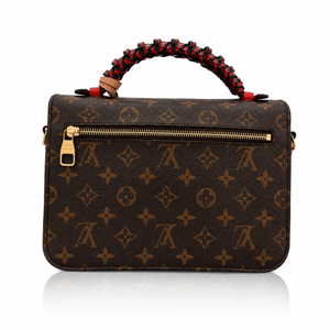 
Louis Vuitton Pochette Métis Crossbody Bag with Braided Handle top handle featuring red and black braided accents, gold-tone hardware, and a front zip closure, shown on a white background with a reflection.