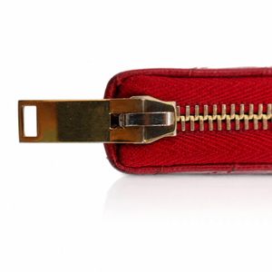 A close-up of a red textured leather zipper pull with a gold-tone metal slider and teeth, set against a plain white background.