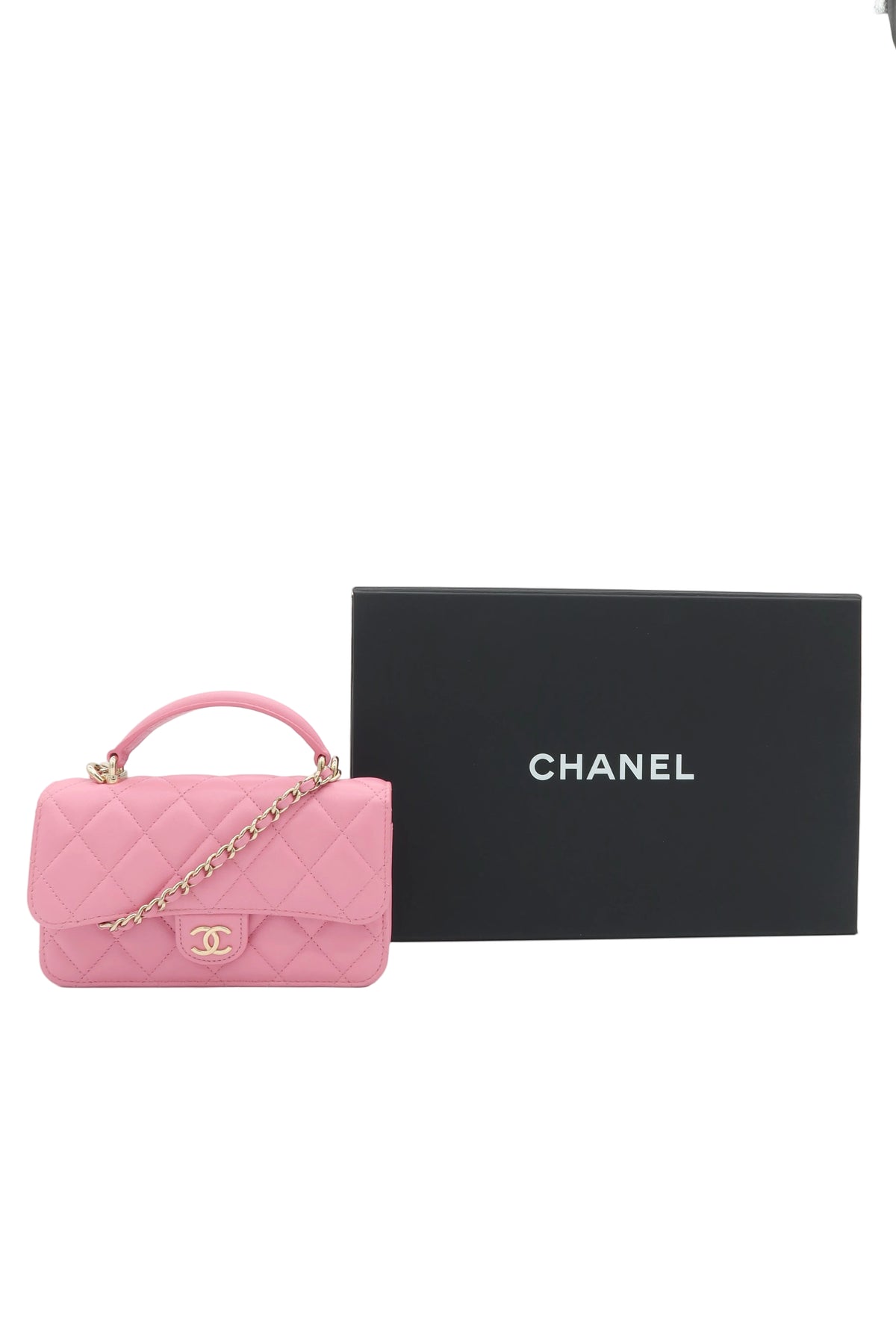 A pink Chanel quilted top-handle handbag with a gold chain strap and CC logo, displayed next to a black Chanel box on a white background.