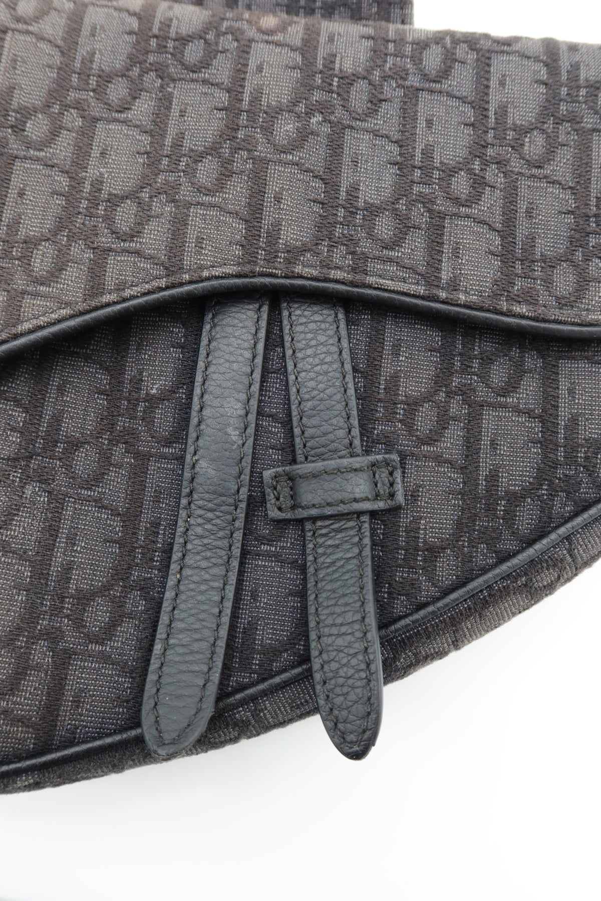 Close-up of a dark gray monogrammed bag with a pebbled leather strap and zipper pull, on a white background.