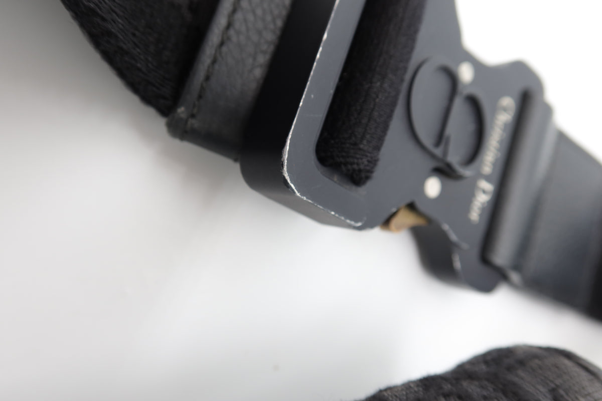 Close-up of a black leather belt with a matte black metal buckle featuring the Gucci logo and 'Gucci London' text, on a white background.